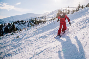 A guy in a red jumpsuit eating freeride on a snowboard on a snowy slope