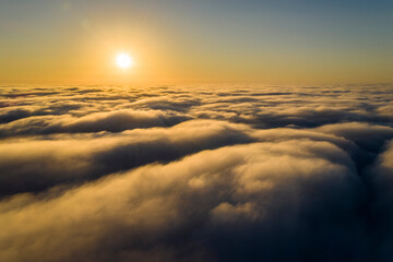 Fototapeta na wymiar Striking aerial view of the sunset sky with the clouds below us. The shadows projected from the Sun passing through the clouds create a dramatical landscape view. Flying above the clouds in the search