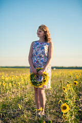 Naklejka na ściany i meble Cute redhaired smiling girl in the field full of sunflowers, wreath of sunflowers.