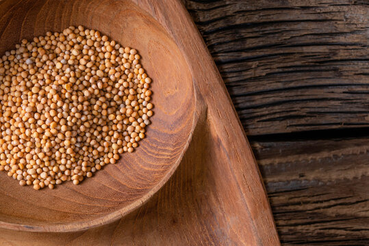 Close up of mustard seeds/Rai or brown mustard seeds in a small plate on a wooden background