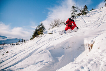 A guy in a red jumpsuit jumps on a snowboard from a snow ledge