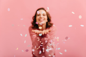 Studio shot of laughing woman with confetti in focus. Brunette girl having fun at party.