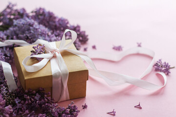 Happy valentines day and mothers day. Lilac flowers, gift box and heart ribbon on pink paper