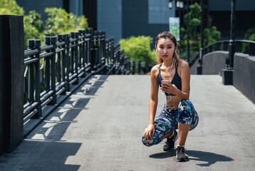 Tired woman taking a break of running, looking at camera and listening music on smartphone