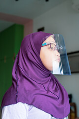 A young girl in hijab wearing the face protection shield. A safety face shield corona mask during Covid-19 pandemic.