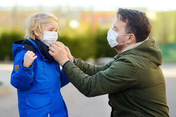 Father wearing a protective mask puts a face mask on a his little son in airport, supermarket or other public place. Safety during COVID-19 epidemic. New strains of coronavirus.