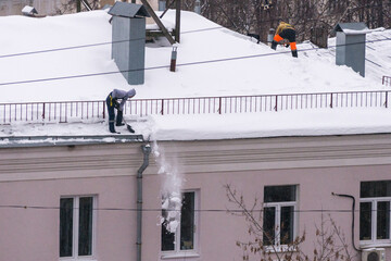 Team of male workers clean roof of building from snow with shovels in securing belts of mantra. - 409034031