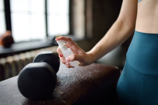 Girl cleaning of sport equipments of gym with disinfecting spray. Woman making disinfection of dumbbells with sanitizer during epidemic. Protection and prevention from infection. - Powered by Adobe