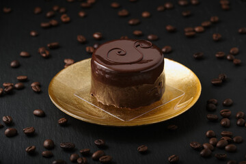 Austrian cake, sackertorte. Chocolate cake on a golden plate. Side view of a chocolate dessert. Coffee beans on a black textured table.