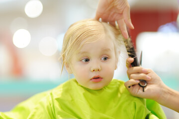 Preschooler boy getting haircut. Children hairdresser with professional tools - comb and scissors.