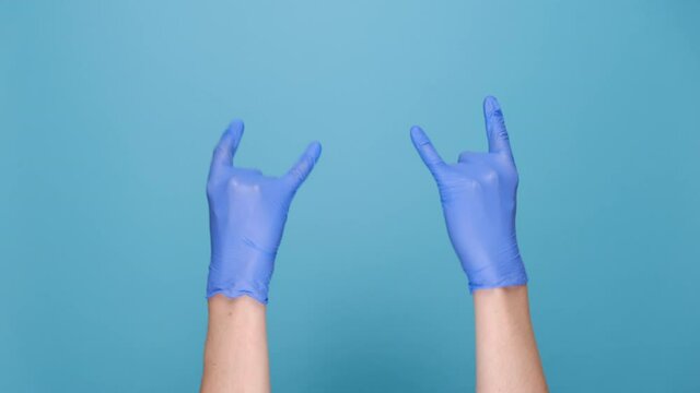 Rock-n-roll and pandemic concept. Male hands in medical protective latex gloves waving with horns gesture, isolated on blue studio background with copy space for advertisement. Body language