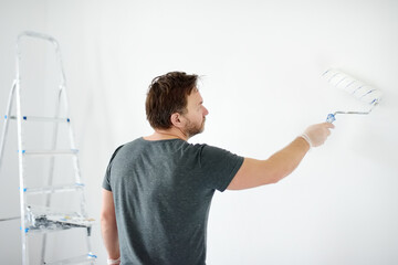 Portrait of a handsome mature man making repairs in the apartment. The person paints the wall white...