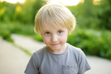 Portrait of a cute green-eyed blonde preschooler boy. Child walking in public park on summer day.
