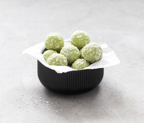 Green tea matcha cottage cheese balls in coconut chips in a bowl on a light gray background