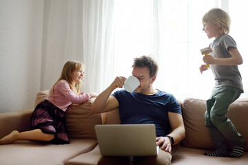 Tired father with his two kids during quarantine. Home office concept. Online working and household...