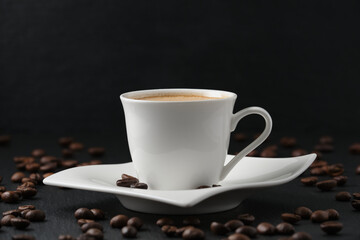 White cup of coffee on a black background. Close-up side view, macro photography. Coffee beans on a black table.