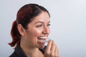Close-up of a woman putting on transparent plastic retainers. The girl uses a device to straighten her teeth