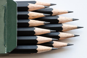 sharp tips of set of black graphite pencils close up in green cartboard box on white background