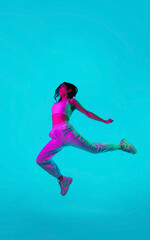Free. Brunette woman's portrait on blue studio background in mixed neon. Beautiful model jumping high, flying with hair blowed out. Concept of human emotions, facial expression, sales, ad, fashion.