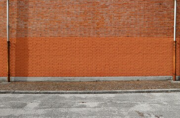 Bicolor brick wall with two gutters at the ends. Porphyry sidewalk and paved road in front. Background for copy space