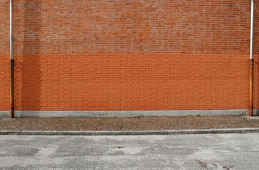 Bicolor brick wall with two gutters at the ends. Porphyry sidewalk and paved road in front....
