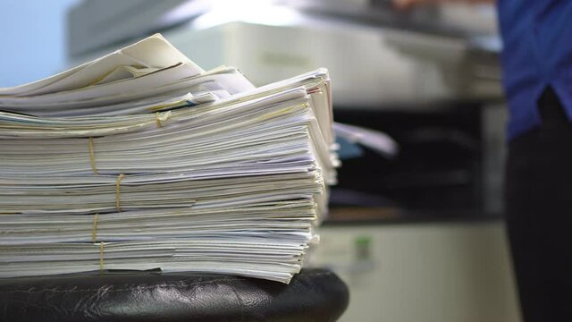 Stack of documents waiting to copy or scan convert to digital data. Blurred of woman is copying or scanning documents.
