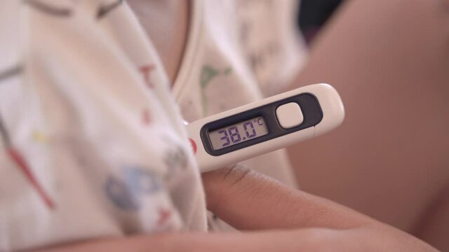 Mother measures body temperature of sad ill little boy with contemporary digital thermometer in light room extreme closeup