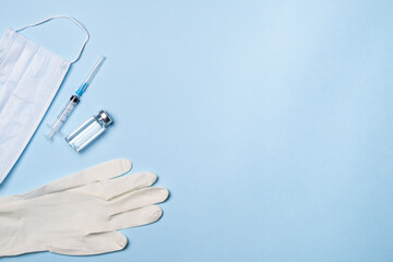 Vials with vaccine, syringe and mask on blue background, flat lay. Space for text. The concept of protection against coronavirus infection, COVID-19, vaccination. Banner