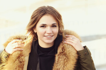  blond business woman in fox fir dawn jacket with hood closeup photo on city park background