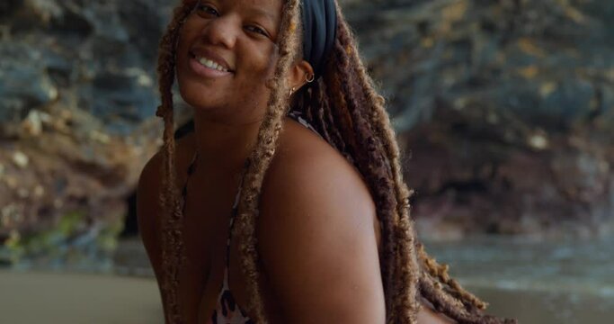 Close up of a girl with dreadlocks smiling and the ocean in the background
