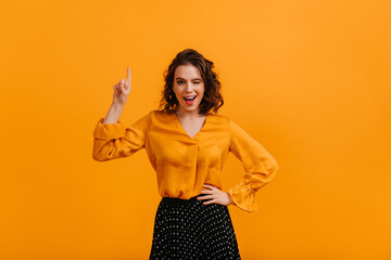 Front view of glad woman pointing with finger. Studio shot of curly girl isolated on yellow background.