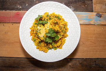 A delicious plate of Indian Curry, Chicken Biriyani topped with green coriander on a wooden kitchen table
