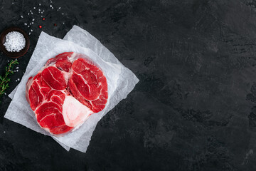 Raw Osso Buco Meat with seasonings on dark stone background.