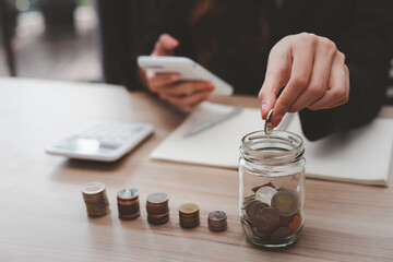 A close-up picture of a business woman putting a coin in a glass jar To save money and plan for it after retirement, money saving ideas And life after retirement