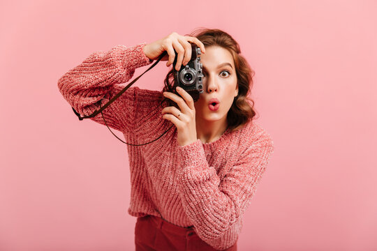 Emotional young lady taking pictures. Studio shot of brunette woman with camera isolated on pink background.