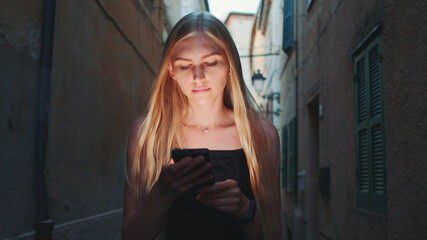 Obraz premium Close-up of blonde woman sharing her impressions from summer trip on video call on smartphone while walking the city of her visit