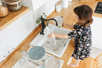 Child girl washing dishes in the kitchen