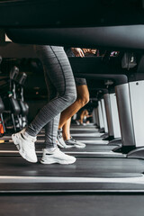 Young fit woman and man running on treadmill in modern fitness gym. Close up shot on moving legs.