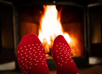 Female feet in red woolen socks by a warm fireplace on a cold winters evening. Shallow depth of field.