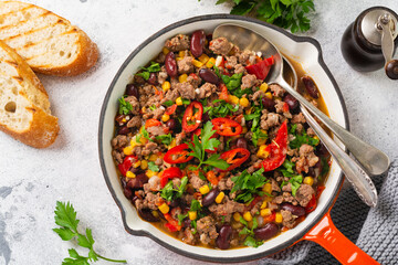 Traditional Mexican food - Chili con carne with minced meat and vegetables stew in tomato sauce in a cast iron pan on light gray slate or concrete background. Top view with copy space.