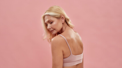 Naklejka premium Natural beauty. Rear view of a beautiful middle aged caucasian blonde lady looking away while posing half naked isolated over pink background