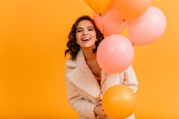Fototapeta na wymiar Attractive young woman holding pink balloons and smiling. Studio shot of blissful birthday girl isolated on yellow background.