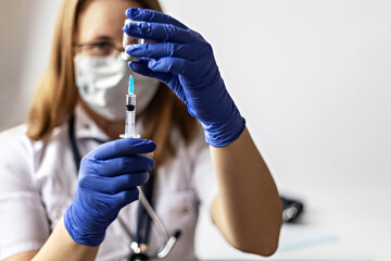 A female doctor wearing a medical mask draws the coronavirus vaccine into a syringe at the clinic.The concept of vaccination, immunization, prevention against Covid-19.