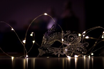 A portrait of a mask lying on a table surrounded by lights. The dark environment casts some mystery...