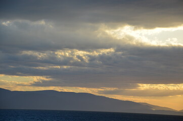 Sunbeams passing through the clouds at sunset. View of the sea and the skyline of the opposite shore.