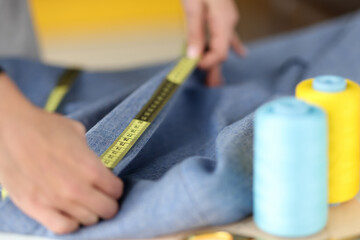 Fototapeta na wymiar Seamstress measuring collar of dress with centimeter tape in sewing workshop