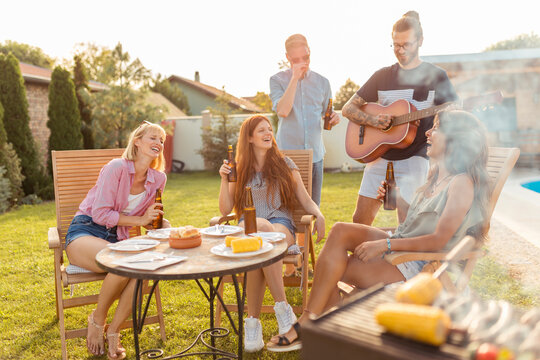 Friends singing and playing the guitar at backyard barbecue party - Powered by Adobe