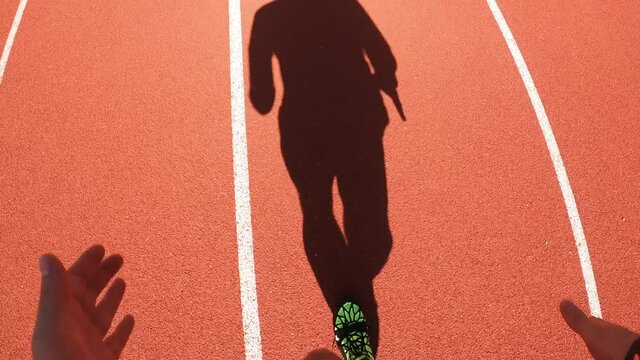 Epic morning shot of unrecognizable male athlete silhouette running and training on stadium. POV shot of running fast on running track.
