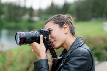Girl photographer european brunette holds a camera and takes pictures on a blurred background of nature.