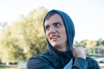 Young attractive blue-eyed man smiling outdoors, wearing hoodie looking to the side on a sunny autumn or spring day on the background of nature